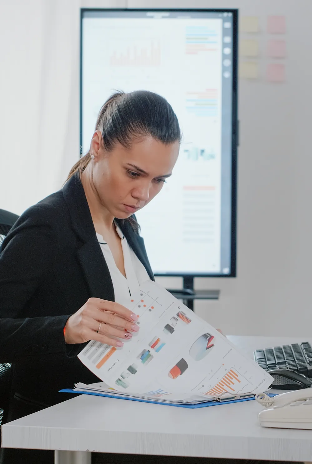 Finance manager reviewing reports with business dashboards on screen behind
